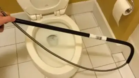 Drain auger cable being fed into a toilet bowl