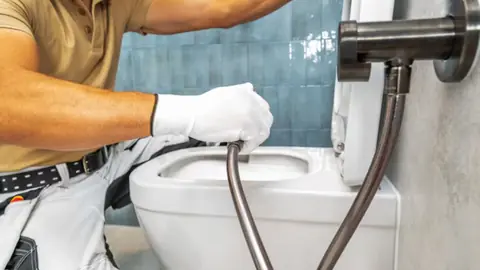 Plumber connecting a braided supply hose to a toilet