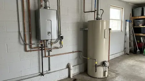 Wall mounted tankless unit next to a tank water heater in a garage