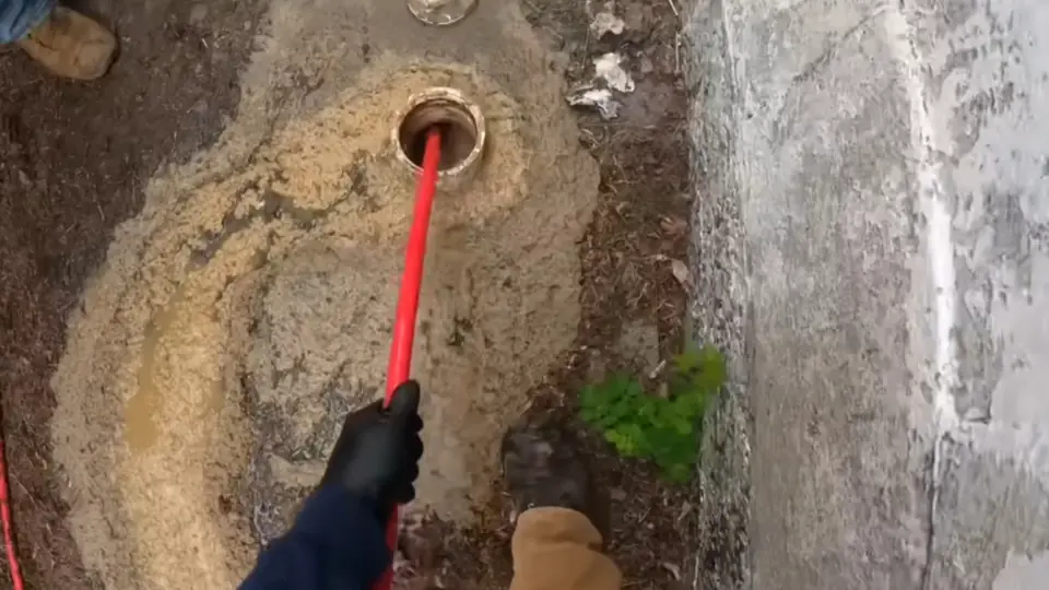 Gloved hand lowering a cleaning tool into a sewer cleanout opening in the ground